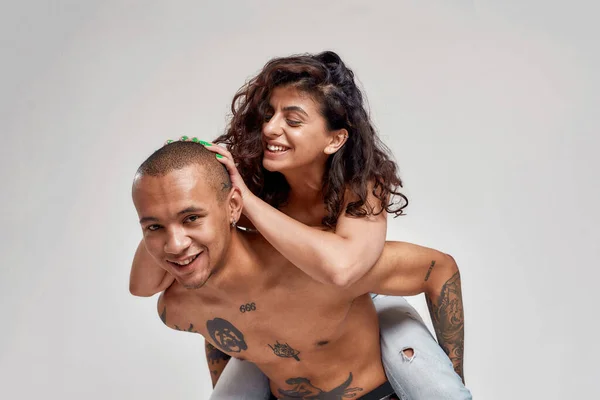 Giovane coppia, tatuato ragazzo e la sua ragazza con ricci capelli scuri divertirsi mentre posa insieme isolato su sfondo grigio — Foto Stock
