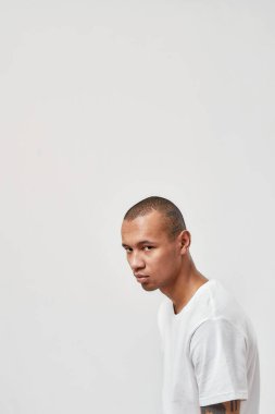 Rahat tişörtlü, beyaz arka planda yalnız poz veren havalı, genç, melez bir adam.