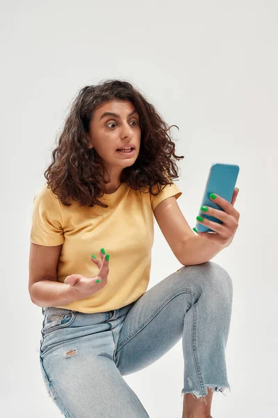 곱슬곱슬 한 검은 머리의 젊은 여자가 셀피 사진을 찍거나 밝은 배경에서 분리 된 스마트폰을 사용하여 비디오 전화를 하는 재밌는 여자 — 스톡 사진