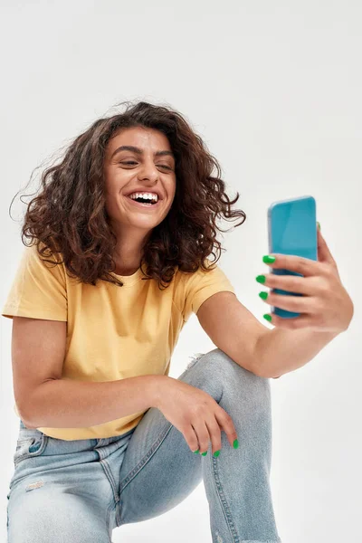 곱슬곱슬 한 검은 머리의 명랑 한 젊은 여성 이 셀카 사진을 찍거나 밝은 배경에서 분리 된 스마트폰을 사용하여 비디오 전화를 하는 모습 — 스톡 사진