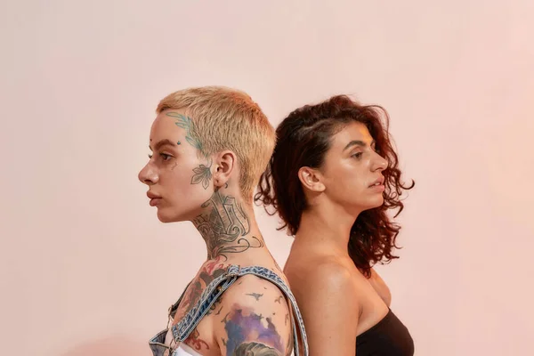 Retrato de duas jovens mulheres diversas, geração Z casal lésbico de pé de volta para trás, posando juntos isolado sobre fundo rosa claro — Fotografia de Stock