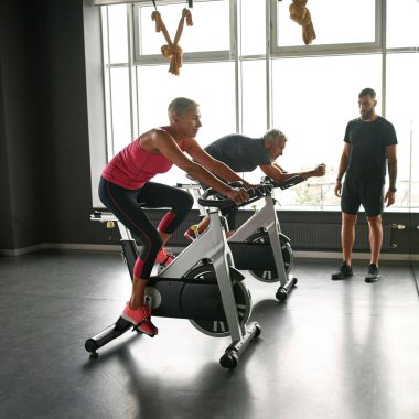 Spor salonunda spor bisikleti kullanan olgun bir çiftin yan görünüşü