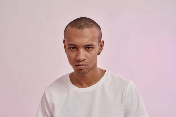 Retrato de focado jovem mestiço homem em casual t-shirt branca olhando para a câmera, de pé isolado sobre fundo rosa — Fotografia de Stock