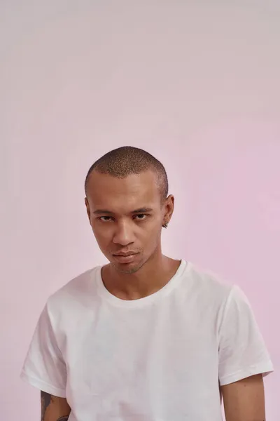 Retrato de grave jovem misto homem de raça em casual t-shirt branca olhando para a câmera, de pé isolado sobre fundo rosa — Fotografia de Stock