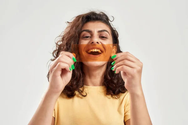 Aufgeregte junge Frau mit orangefarbenem Film vor dem Mund posiert isoliert vor hellem Hintergrund — Stockfoto