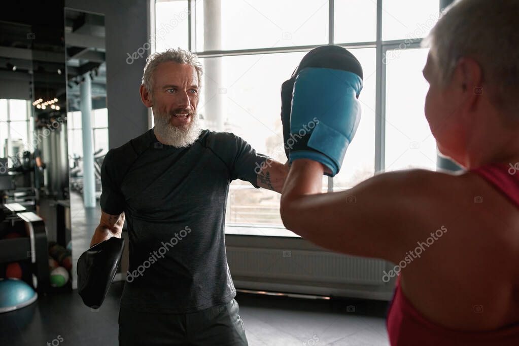 Active mature boxing trainer teaching women self-defence techniques