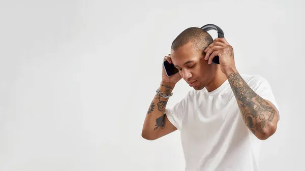 Jóvenes tatuados de raza mixta enfocados usando auriculares, escuchando música hip hop mientras posan aislados sobre un fondo blanco —  Fotos de Stock