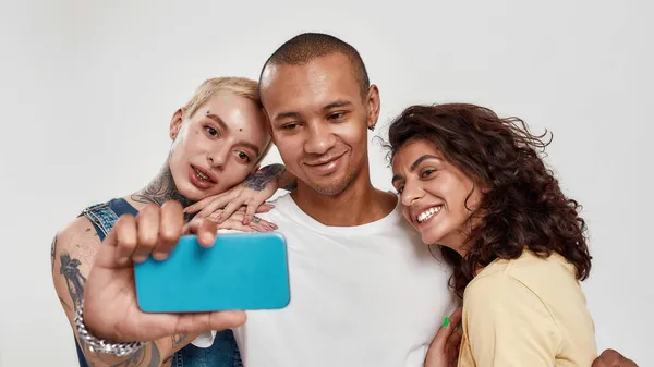Carino giovani diverse persone in abbigliamento casual utilizzando smartphone, prendendo selfie, in piedi insieme isolati su sfondo chiaro — Foto Stock