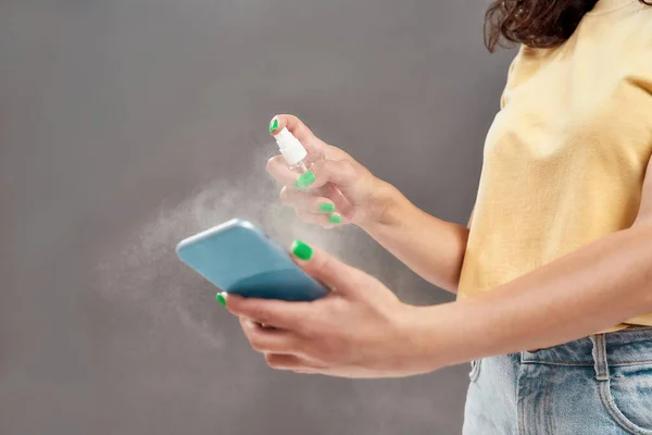 Foto recortada de mujer que aplica aerosol de alcohol desinfectante en su teléfono inteligente para la desinfección aislada sobre fondo gris — Foto de Stock