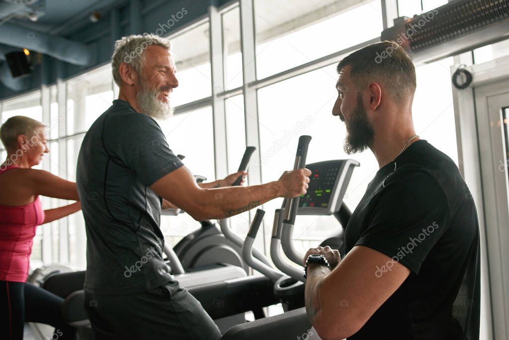 Cheerful mature man happily chatting with trainer while exercising