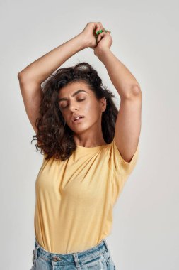 Esmer, kıvırcık saçlı, rahat bir manken. Gri arka planda kapalı gözlerle poz veriyor.