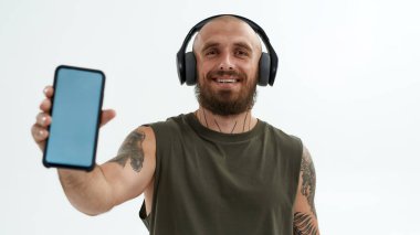 Kulaklıklı genç adam akıllı telefon gösteriyor.