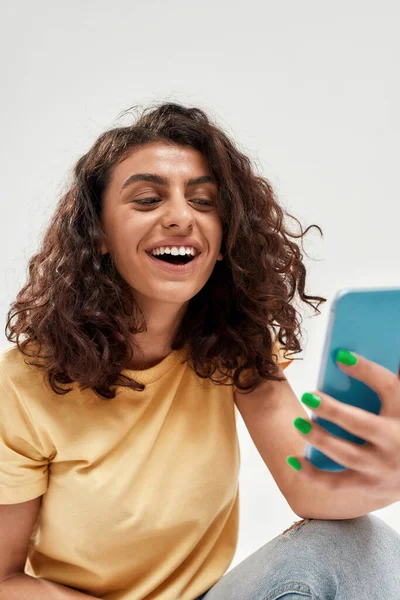 밝은 배경 위로 분리 된 스마트폰을 사용하여 비디오 전화를 하는 동안 곱슬머리가 검은 행복 한 젊은 여성 — 스톡 사진