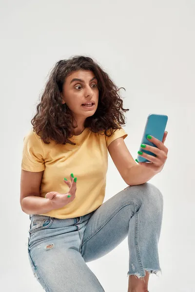 Mujer joven divertida con el pelo oscuro rizado haciendo foto selfie o haciendo videollamada usando teléfono inteligente aislado sobre fondo claro — Foto de Stock