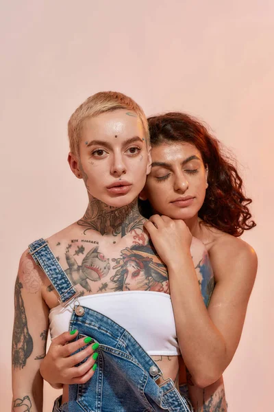 Giovani donne diverse, generazione Z coppia lesbica abbracciando mentre posa insieme isolato su sfondo rosa chiaro — Foto Stock