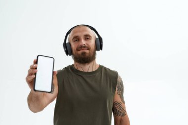 Kulaklıklı adam kameraya akıllı telefon gösteriyor.