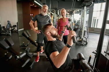 Atletizm antrenörü, spor aletlerinin nasıl kullanılacağını gösteriyor
