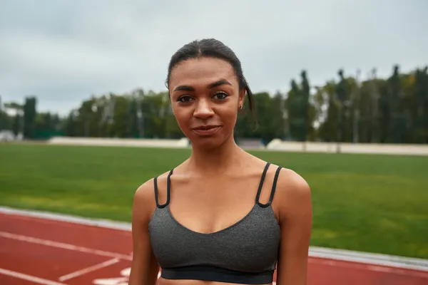 Sonriente mujer de los deportes negros en la cinta de correr del estadio — Foto de Stock
