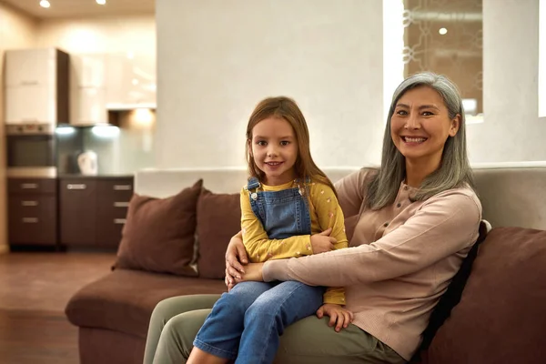 Fürsorgliche Kindermädchen und schöne Mädchen sitzen auf dem Sofa — Stockfoto