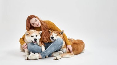 Gülümseyen kadın oturuyor ve Shiba Inu köpeklerine sarılıyor.