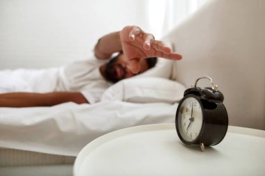 Yatakta uyurken çalar saati durduran adam.