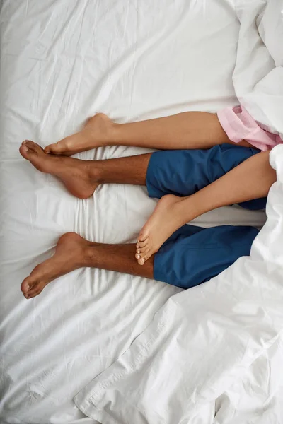 Pernas de homem preto e mulher sob cobertor na cama — Fotografia de Stock