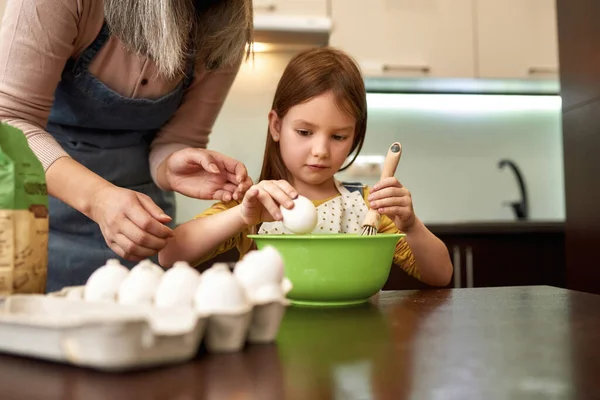 Mädchen bricht beim Kochen mit Großmutter Ei — Stockfoto