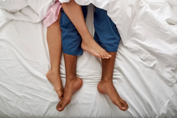 Ben av svart man och flicka under filt på sängen — Stockfoto