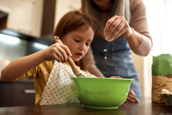 Mädchen, das Teig mixt und Oma gießt Mehl in Schüssel — Stockfoto