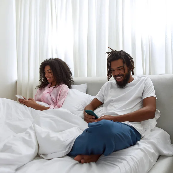 Negro pareja descansar y ver en los teléfonos inteligentes en la cama —  Fotos de Stock