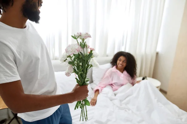 Man med bukett blommor nära flickvän i sängen — Stockfoto