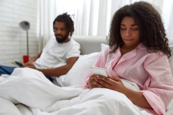 Μαύρο ζευγάρι που ξεκουράζεται και χρησιμοποιεί smartphones στο κρεβάτι — Φωτογραφία Αρχείου