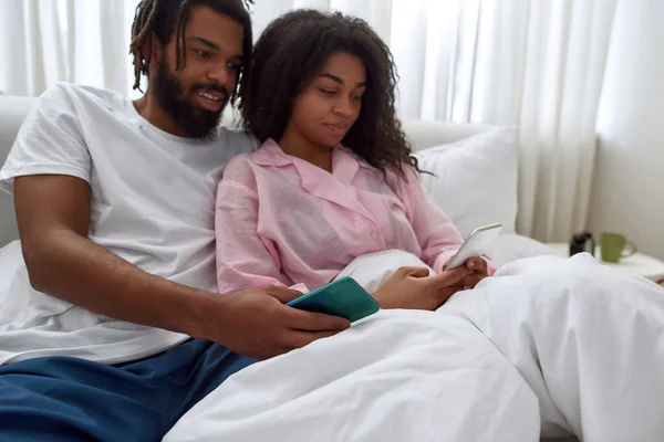 Joven pareja negra viendo en el teléfono inteligente en la cama —  Fotos de Stock