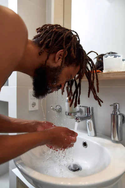 Black man washing face in wash basin in bathroom