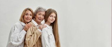 Sırt sırta üç dişiden oluşan gülümseyen bir aile