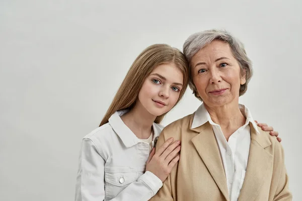 Внучка обнимает пожилую женщину на белом фоне — стоковое фото