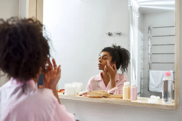 Black woman applying cosmetic cream on her face