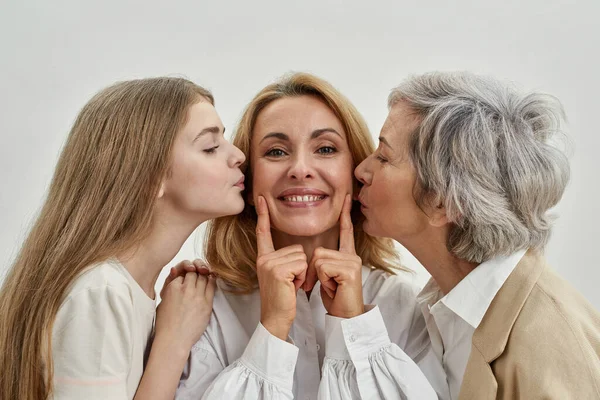 Genç bir kız ve yaşlı bir kadın yetişkin bir kadını öper.