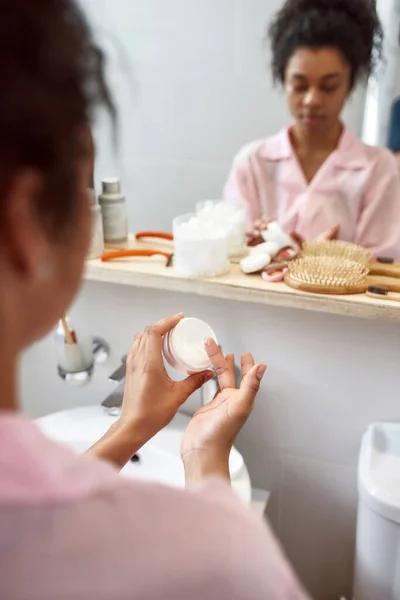 Mujer negra tomando crema cosmética en el baño — Foto de Stock