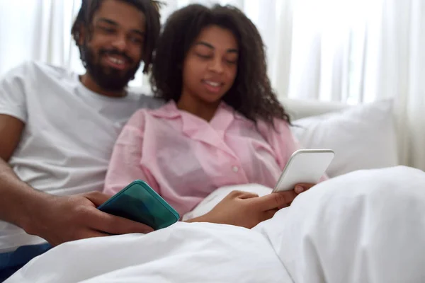 Desenfoque de la pareja negra viendo en el teléfono inteligente en la cama —  Fotos de Stock