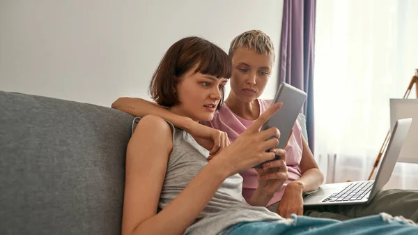 Focused lesbians watch on digital tablet on sofa — Fotografia de Stock