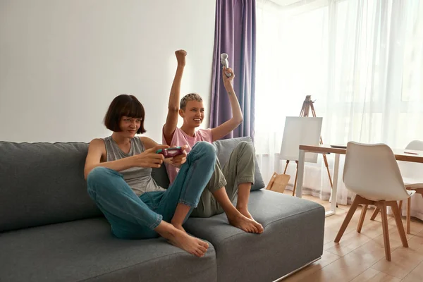 Lesbian girls playing video game on sofa at home — Fotografia de Stock