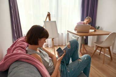 Kız akıllı telefon ve kız arkadaş masasında çalışıyor.