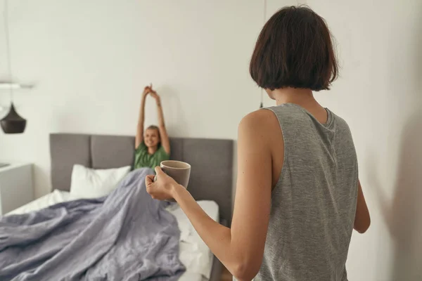 Вид ззаду дівчина носить чай з дівчиною в ліжку — стокове фото