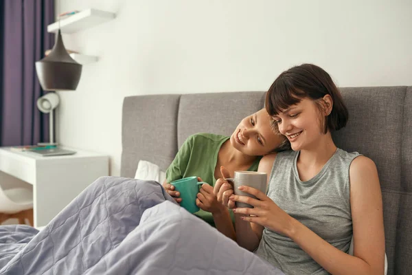 Smiling lesbians resting and drinking tea on bed — Foto Stock