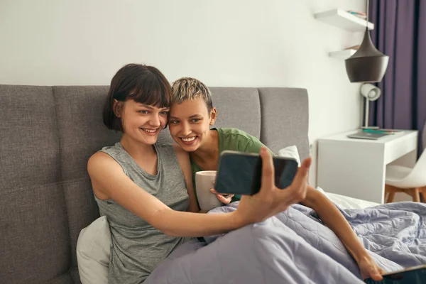 Lesbianas toman selfie en smartphone en la cama en casa —  Fotos de Stock