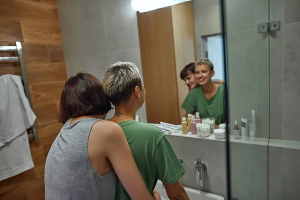 Lesbian girls hug and look in mirror at bathroom — Zdjęcie stockowe