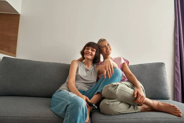 Young smiling lesbian girls watching TV on sofa — Foto Stock