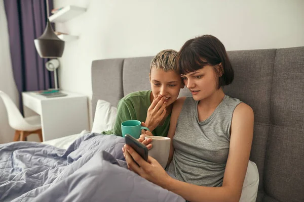 Young lesbians watching on smartphone on bed — Fotografia de Stock