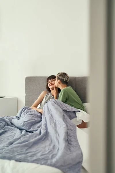 Chica besando a su novia sonriente en la cama en casa —  Fotos de Stock